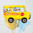 A yellow foil balloon shaped like a school bus with cartoon animal passengers visible through the windows, plus a stop sign graphic and ribbons, shown against a light gray paneled background.