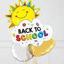 A set of back-to-school foil balloons including a smiling yellow sun, a white cloud-shaped balloon with 'BACK TO SCHOOL' text, and a gold heart balloon, shown against a light gray paneled wall.