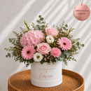 A personalized flower arrangement in a white cylindrical pot with the text 'ON YOUR DADS Emma' printed in rose gold. The bouquet features pink hydrangeas, pink and white roses, pink gerbera daisies, white ranunculus, and green eucalyptus leaves.